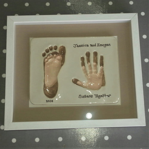 Rectangle Clay Imprint with small foot and hand print inside older sibling's foot and hand print.  Small prints in off white and larger print in beige with beige backboard and white frame. 