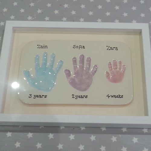 Rectangle Clay Imprint with three sibling hand prints in blue, lilac and pink with off white back board and white frame.