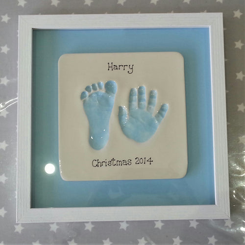 Clay Imprint with a foot and hand print in pastel blue with pastel blue backboard and white frame.