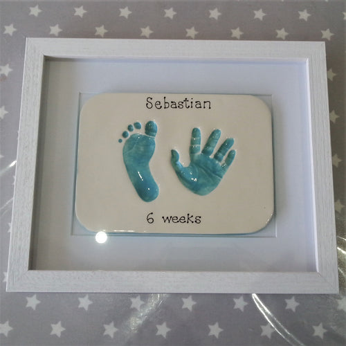 Rectangle clay imprint with foot and hand print in teal with white backboard and white frame. 