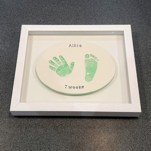 Oval Clay Imprint with a hand and footprint in mint green with white backboard and white frame.