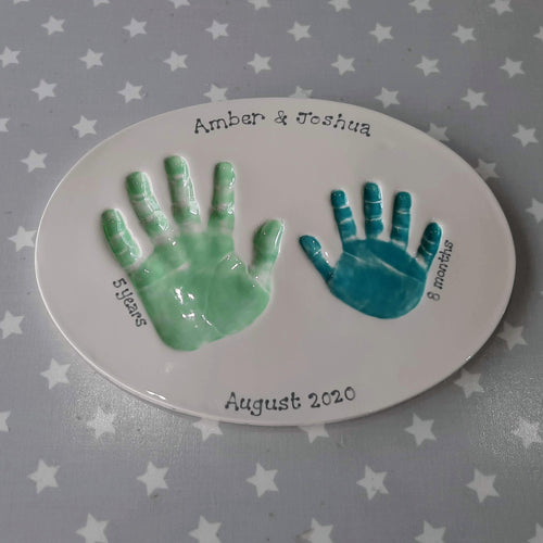 Oval Clay Imprint with two siblings hand prints. Larger hand in mint green and smaller hand in teal.  Unframed.