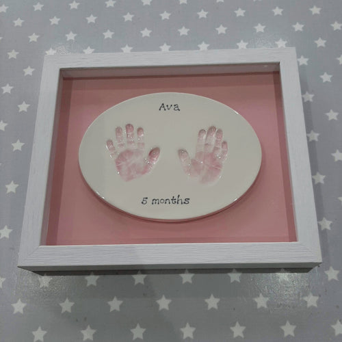 Oval Clay Imprint with two hands. Prints painted in pastel pink with pink back board and white frame.