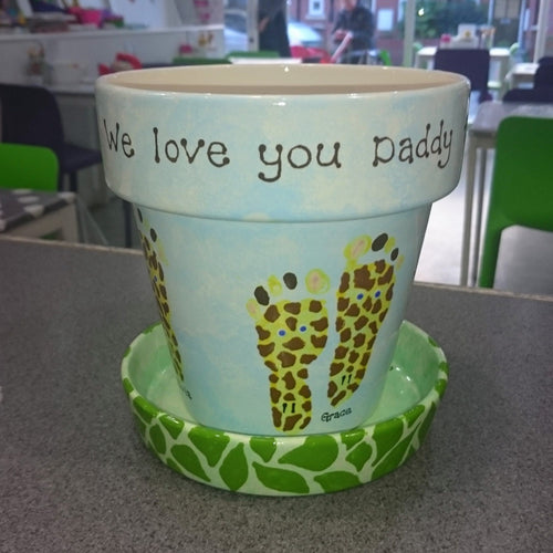 Large Plant Pot with two yellow footprints decorated to look like giraffes.  Plant pot base decorated with green camouflage, as a gift for Daddy.