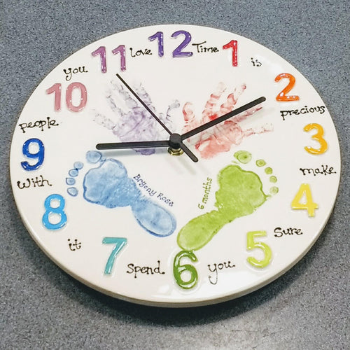 Hand prints and footprints on round clock with brightly painted numbers.