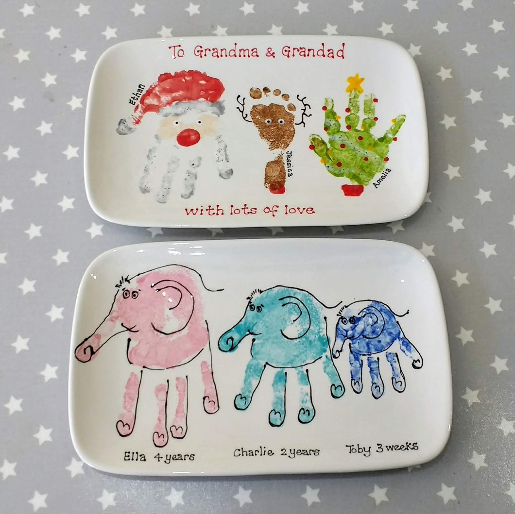 Two personalised, rectangle plates, one with a Santa hand print, Rudolph footprint and Christmas Tree hand print.  One with three Elephant hand prints in pink, teal and blue.