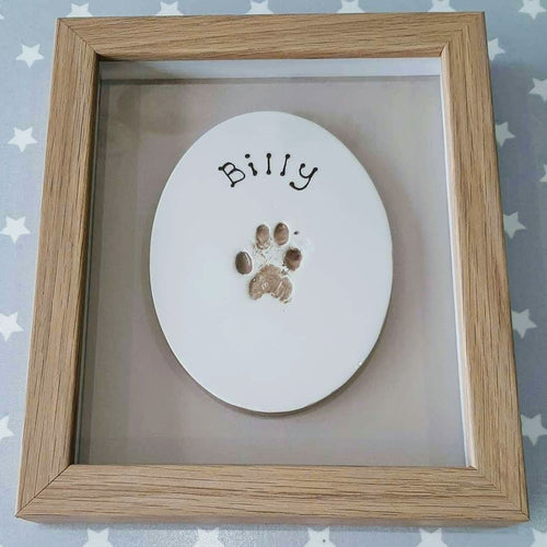 Oval Clay Imprint with pet paw print in beige with beige backboard and wooden frame.