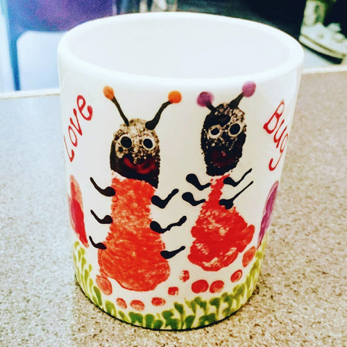 Black and red footprints turned into ladybirds with grass design on a regular mug, with Love Bug wording.