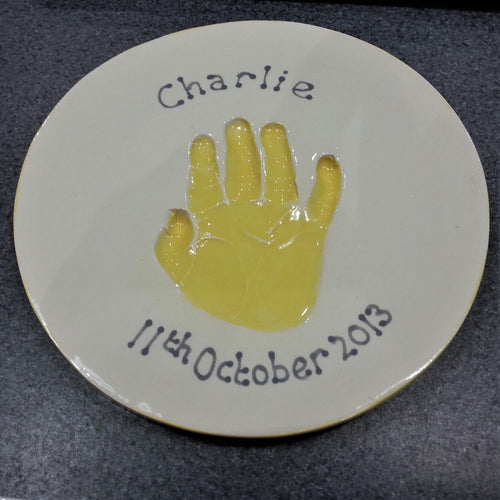 Round Clay Imprint with single hand print in yellow.  Unframed. 