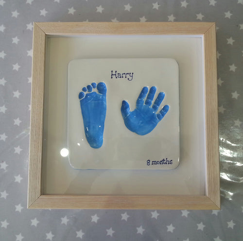 Square Clay Imprint with foot and hand print in blue with white back board and wooden frame.