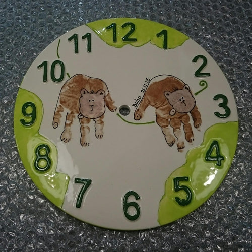 Brown hand prints turned into monkeys on a clock with green painted numbers and tree scene.
