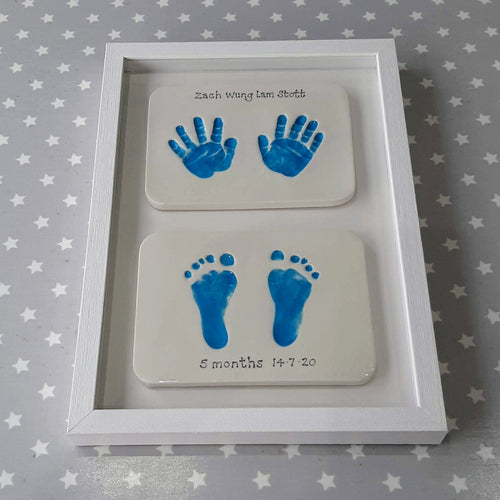 Two rectangle Clay Imprints, one with two hand prints and one with two footprints.  Prints in blue framed together with white backboard and white frame. 