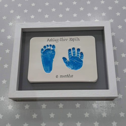 Rectangle Clay Imprint with a foot and hand print in blue with grey back board and white frame.