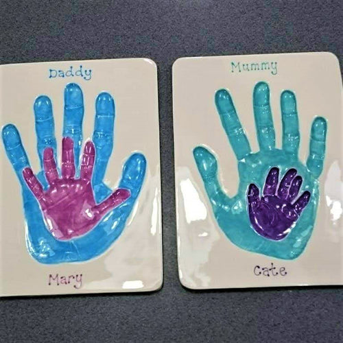 Two rectangle Clay Imprints with smaller children's hand prints inside larger parents hand prints.  Children's prints in pink and purple, parents prints in blue and teal. Unframed. 