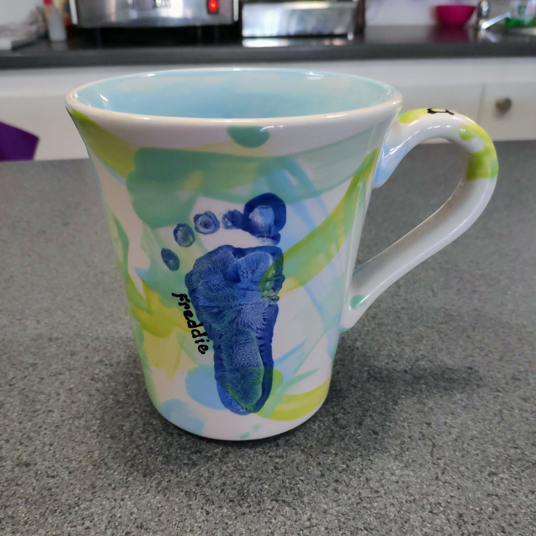 A painted footprint on a mug, decorated with lighter colours before the print was taken.  This is the mug, after it has been glazed and fired in the kiln.