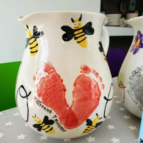 Traditional Jug with two red footprints positioned to make the letter V in the word LOVE, decorated with painted bees. 