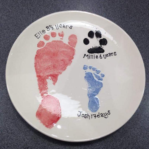 A medium coupe plate with a red footprint, younger sibling's blue footprint and their pet's paw print in black.